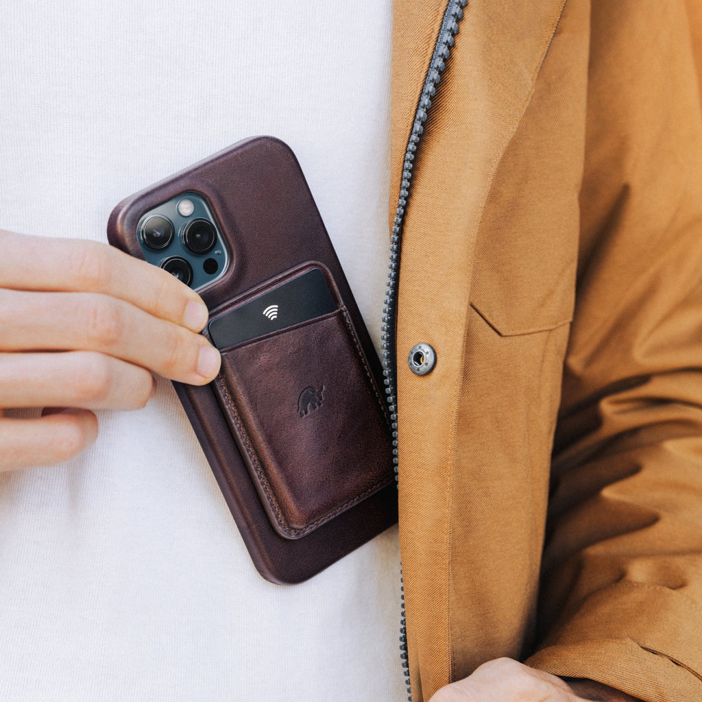A person placing a bourbon leather magnetic wallet into a jacket pocket with a phone visible.
