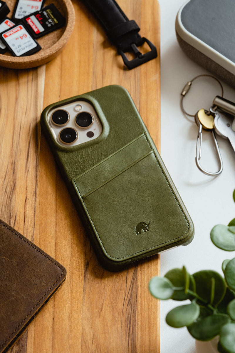 Green leather iPhone case with card pocket on wood surface; keys and SD cards labeled SanDisk Ultra 64GB nearby