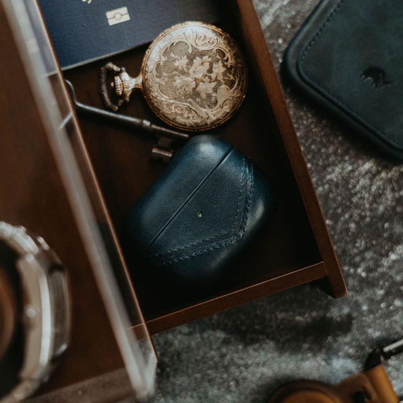 Leather AirPods case in a drawer with a pocket watch and key.