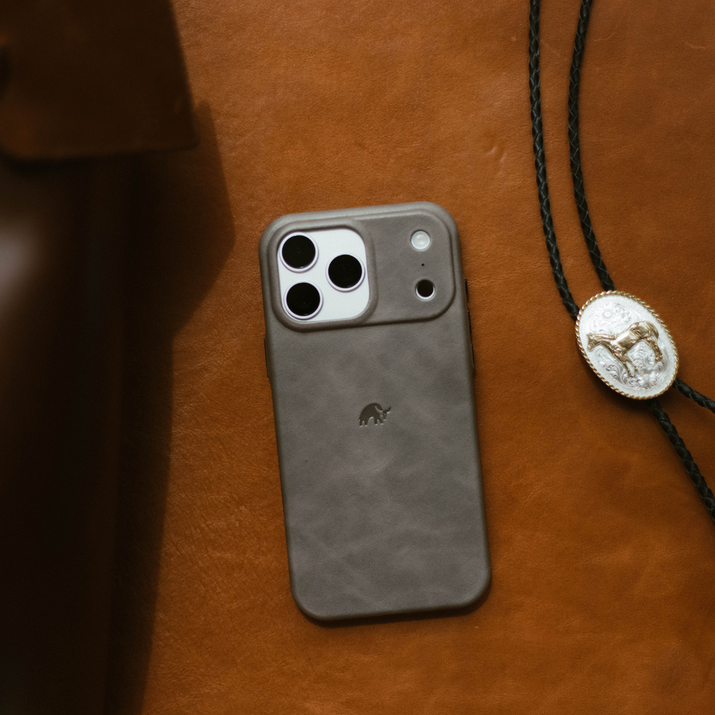 Gray leather iPhone case with triple-camera cutouts and small elephant logo on brown leather background.