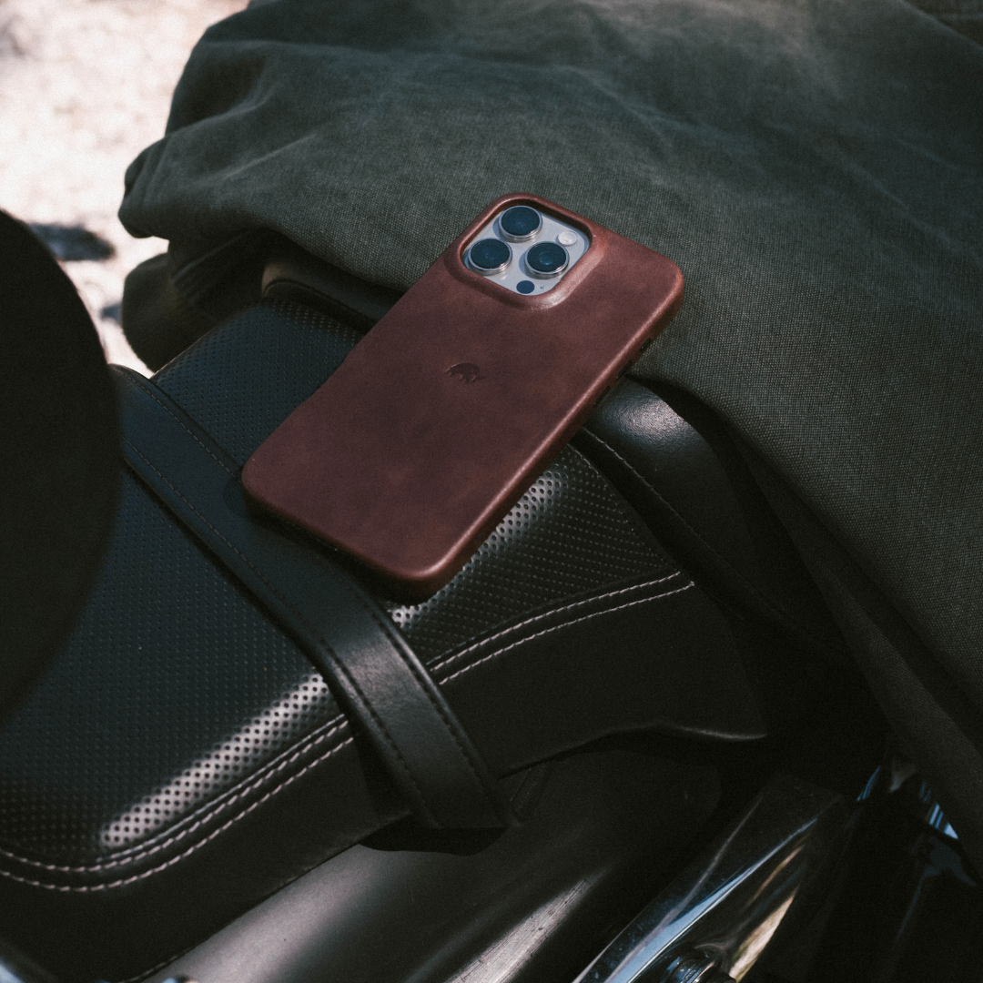 Minimalist leather phone case in bourbon brown resting on a black motorcycle seat
