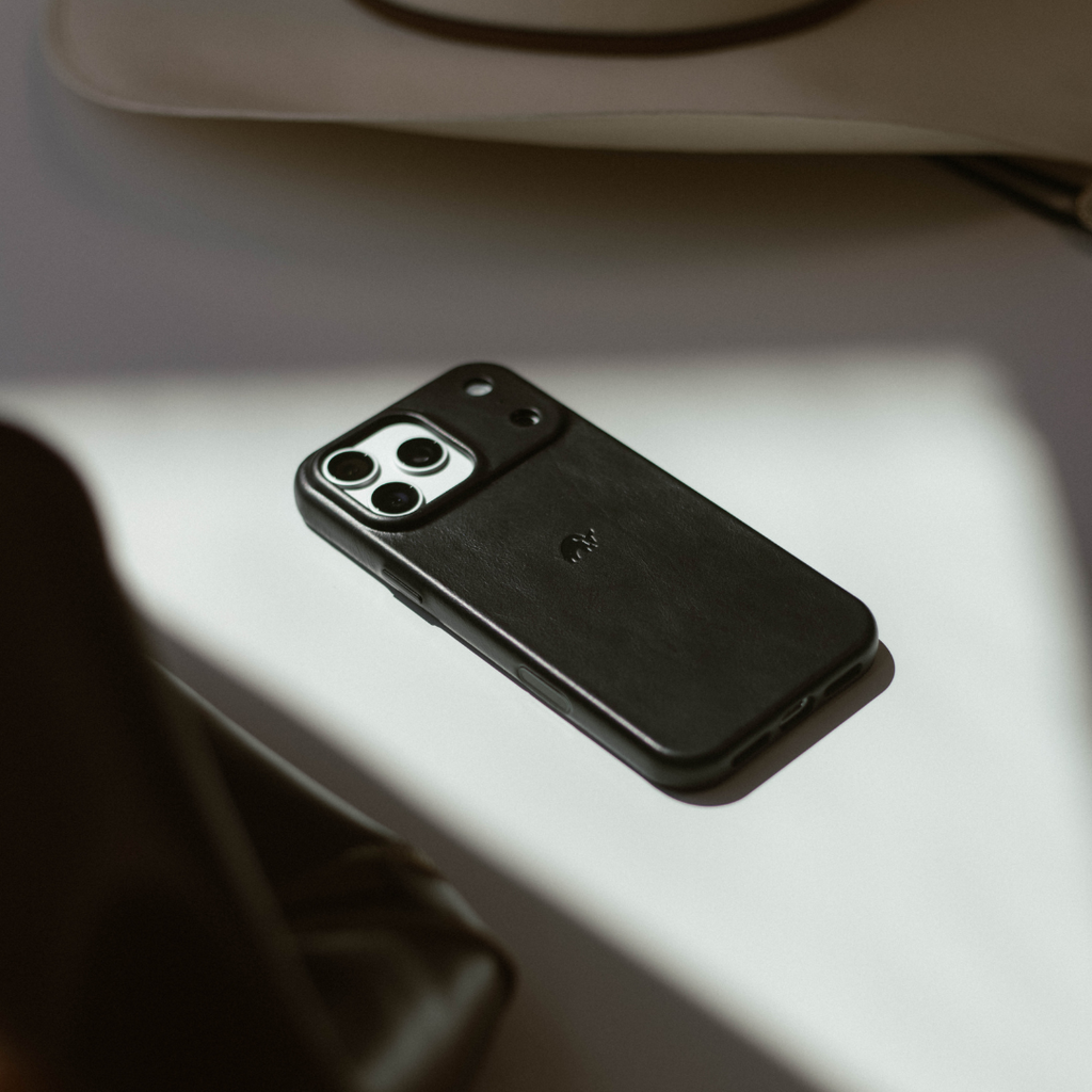 Black leather phone case on tabletop showing camera cutout, soft directional light and shadow