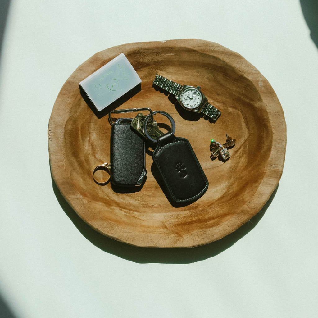 Overhead view of Trace Trackable Keychain in black showing leather pouch with embossed logo and keyring on wooden dish