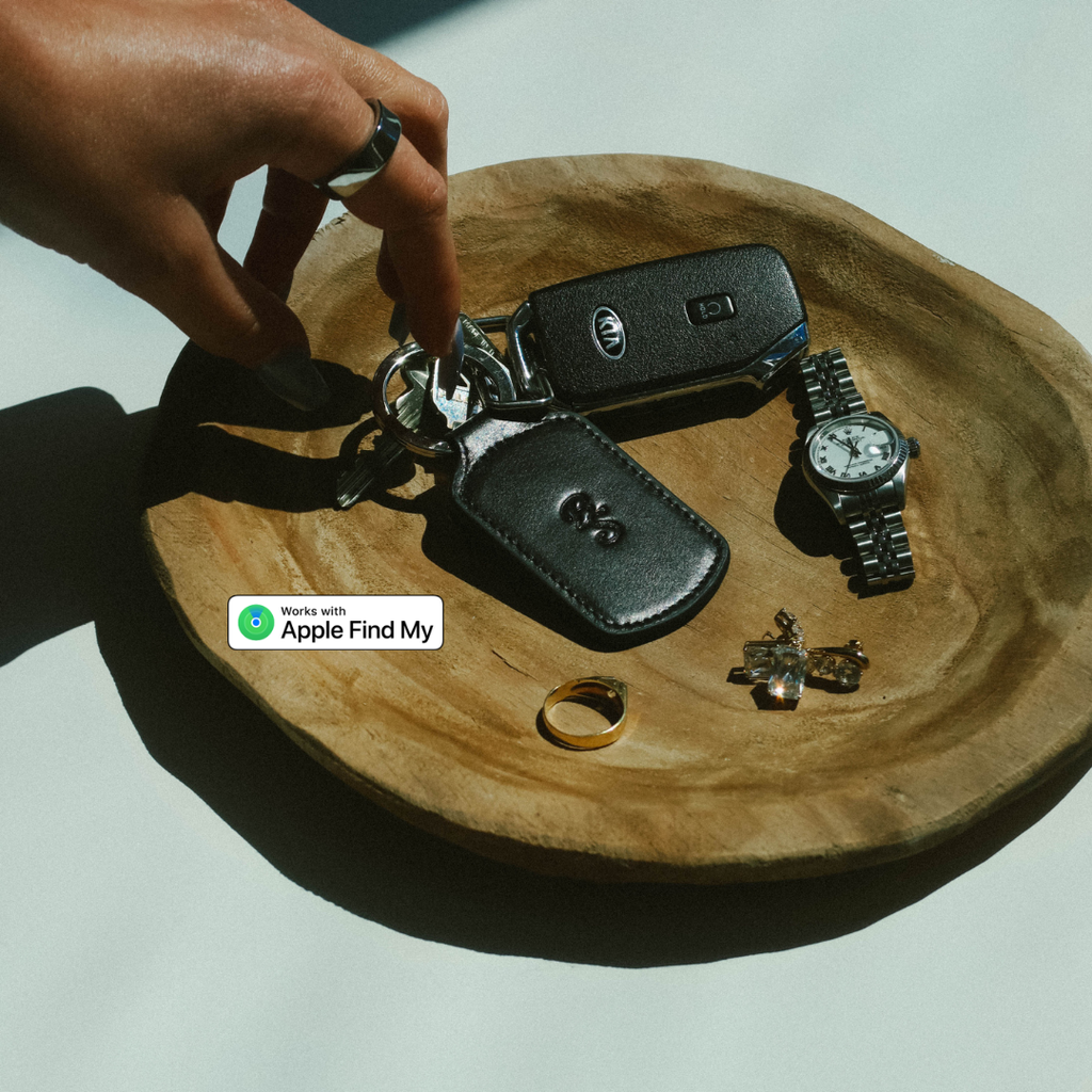 Top view of black Trace Trackable Keychain in leather with Works with Apple Find My badge on a wooden dish with keys