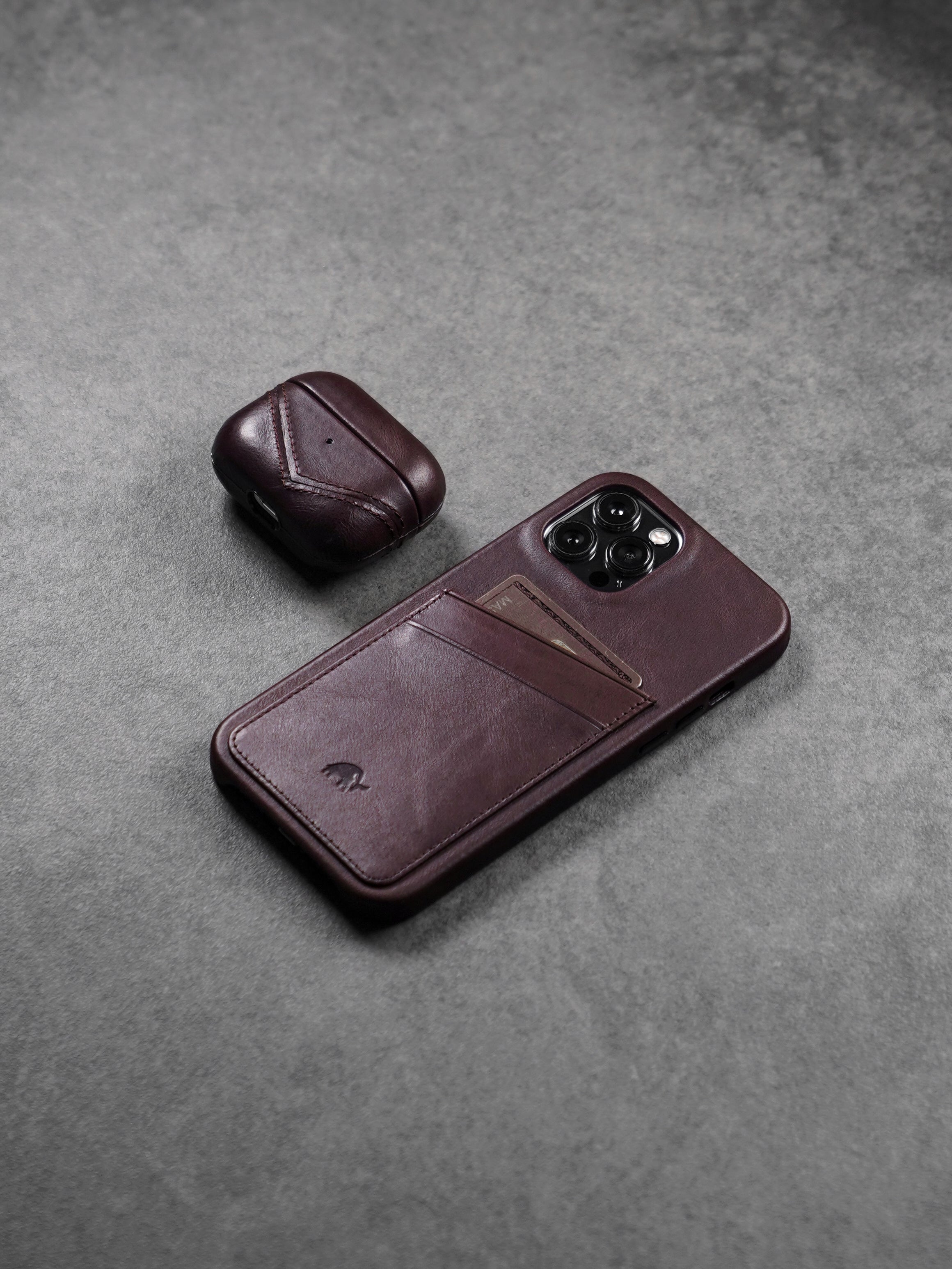 Leather phone case with card slot and matching AirPods case on a gray surface.