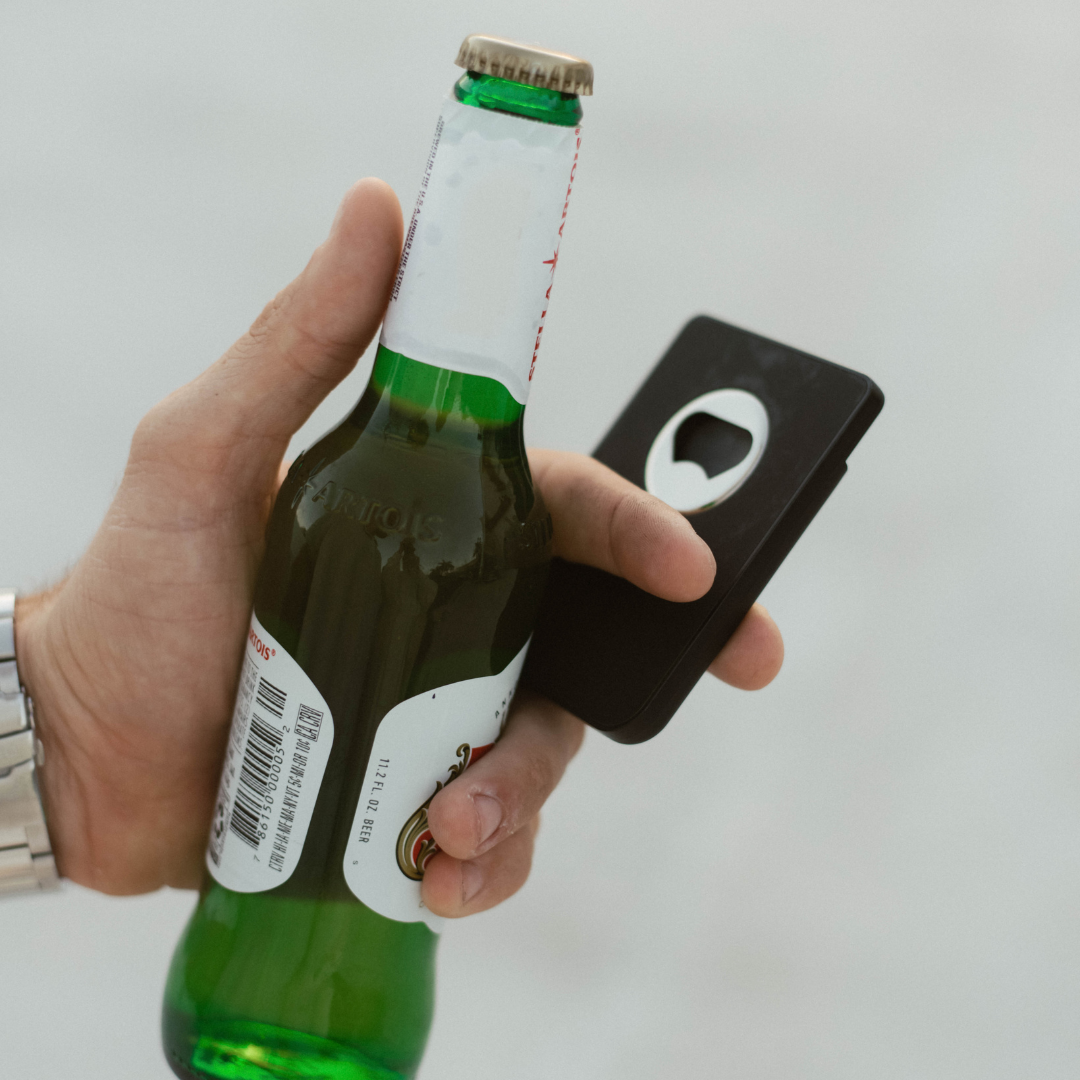 A hand holding a beer bottle and a wallet with a built-in bottle opener.