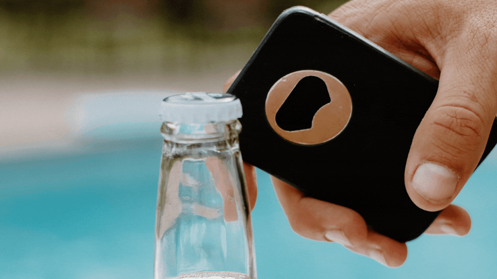 A hand using a bottle opener on a glass bottle cap.
