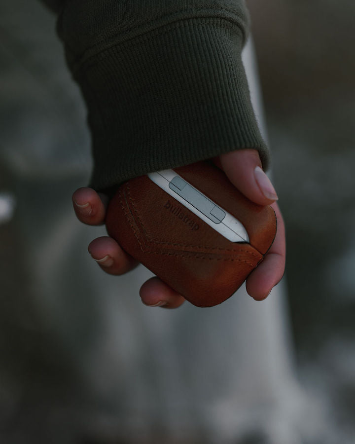 A person holding a Bullstrap leather AirPods case in their hand.