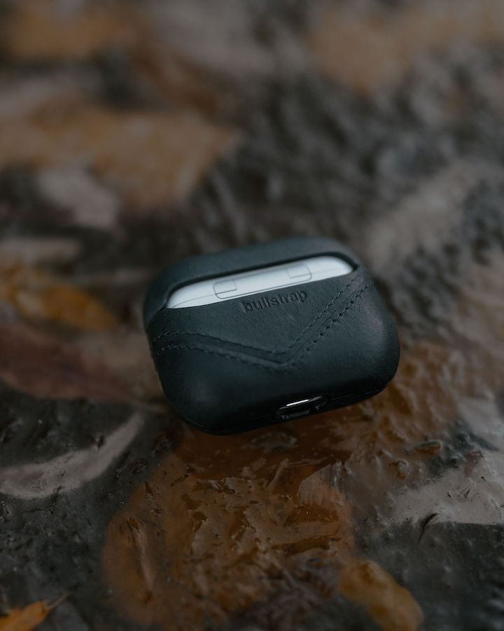 Black leather AirPods case with embossed Bullstrap logo on a textured surface.