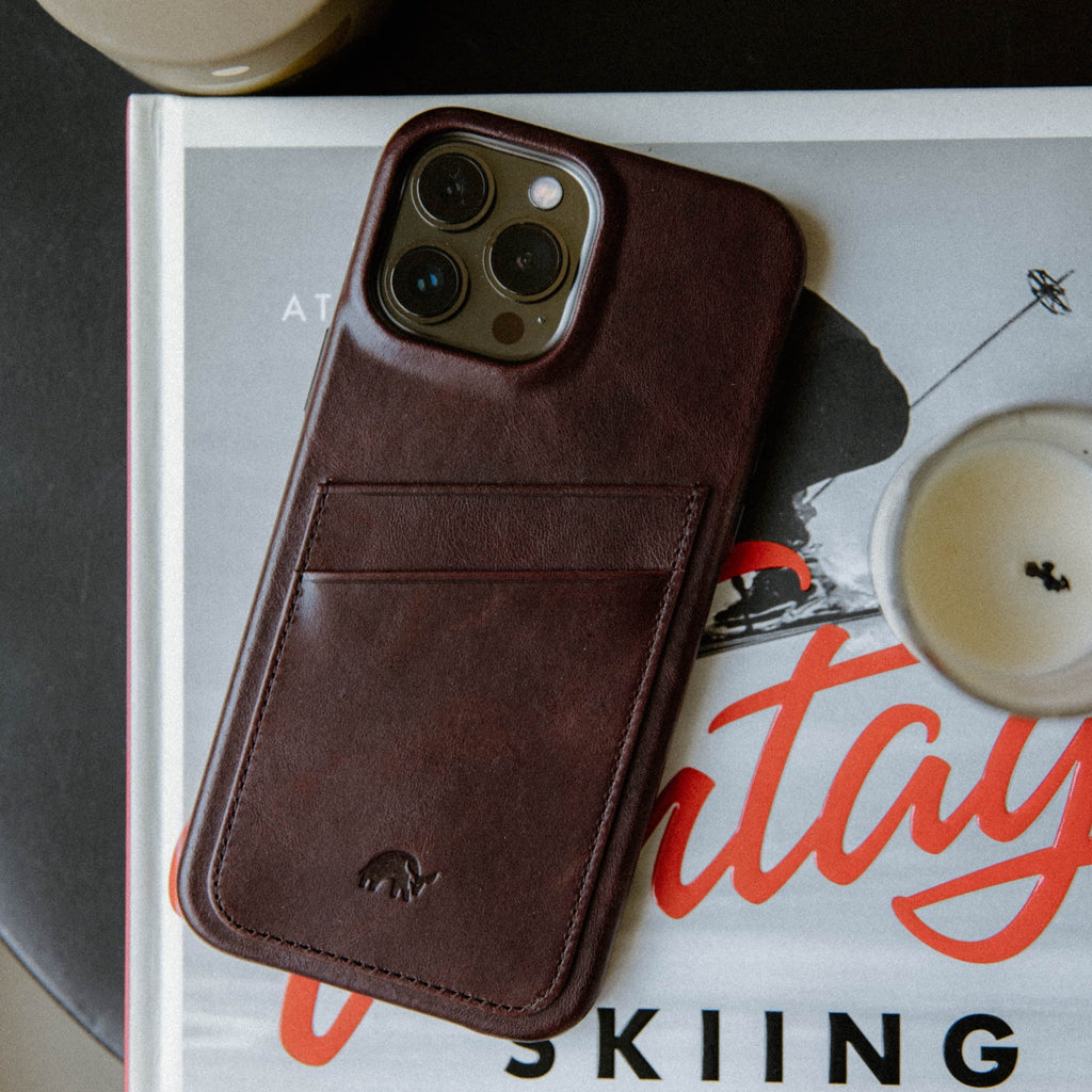 The Minimalist Portfolio Case in Bourbon color, featuring a card slot, placed on a book with a candle nearby.