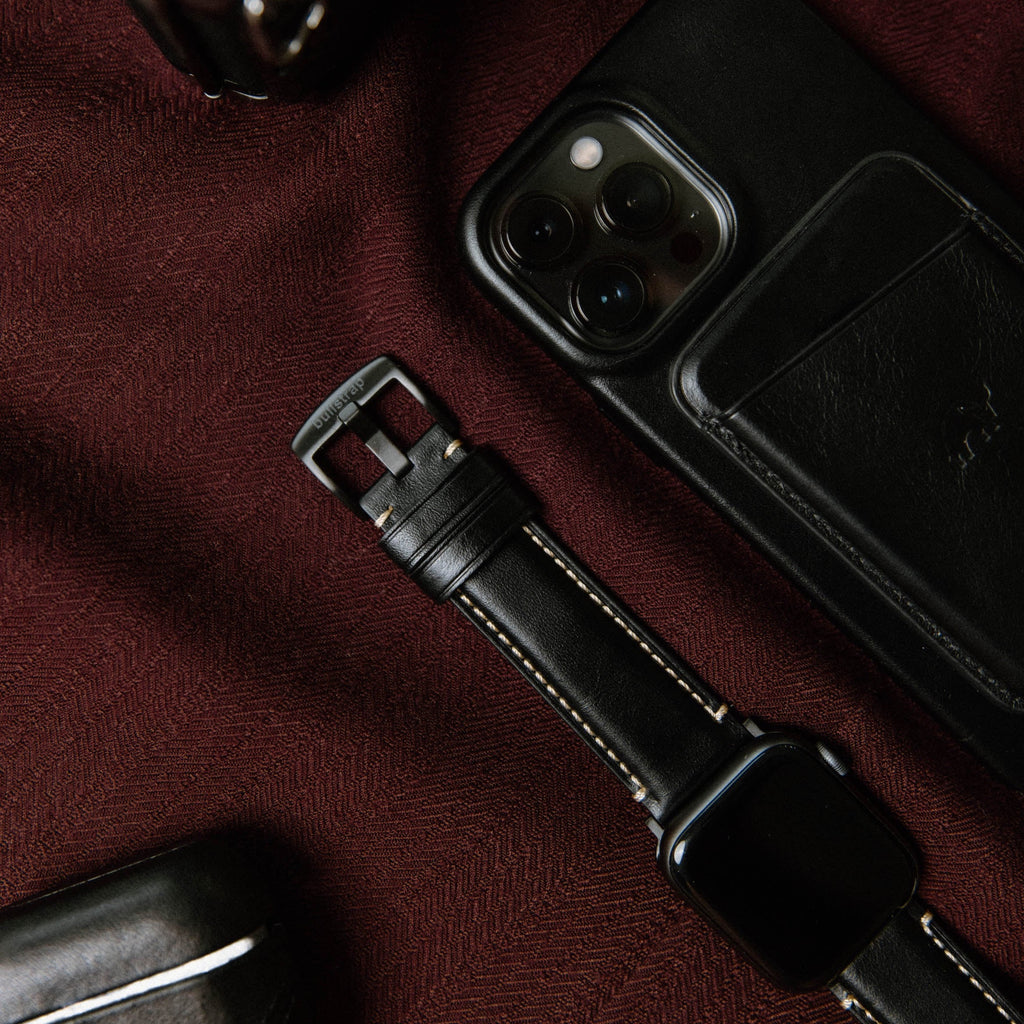 Close-up of a black leather Apple Watch strap next to a phone and wallet.