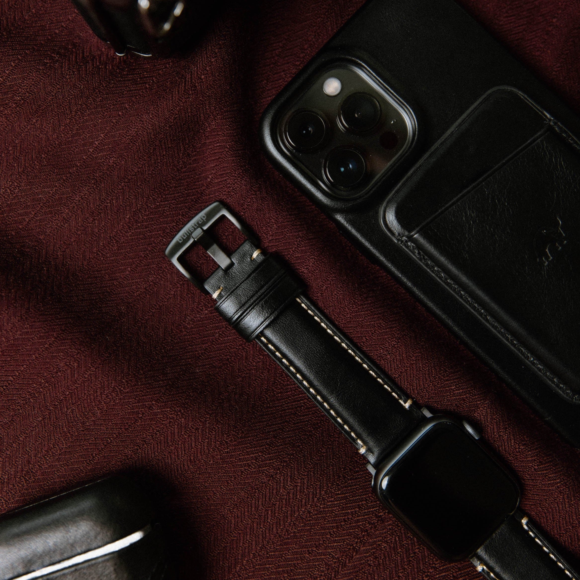 Close-up of a black leather Apple Watch strap next to a phone and wallet.
