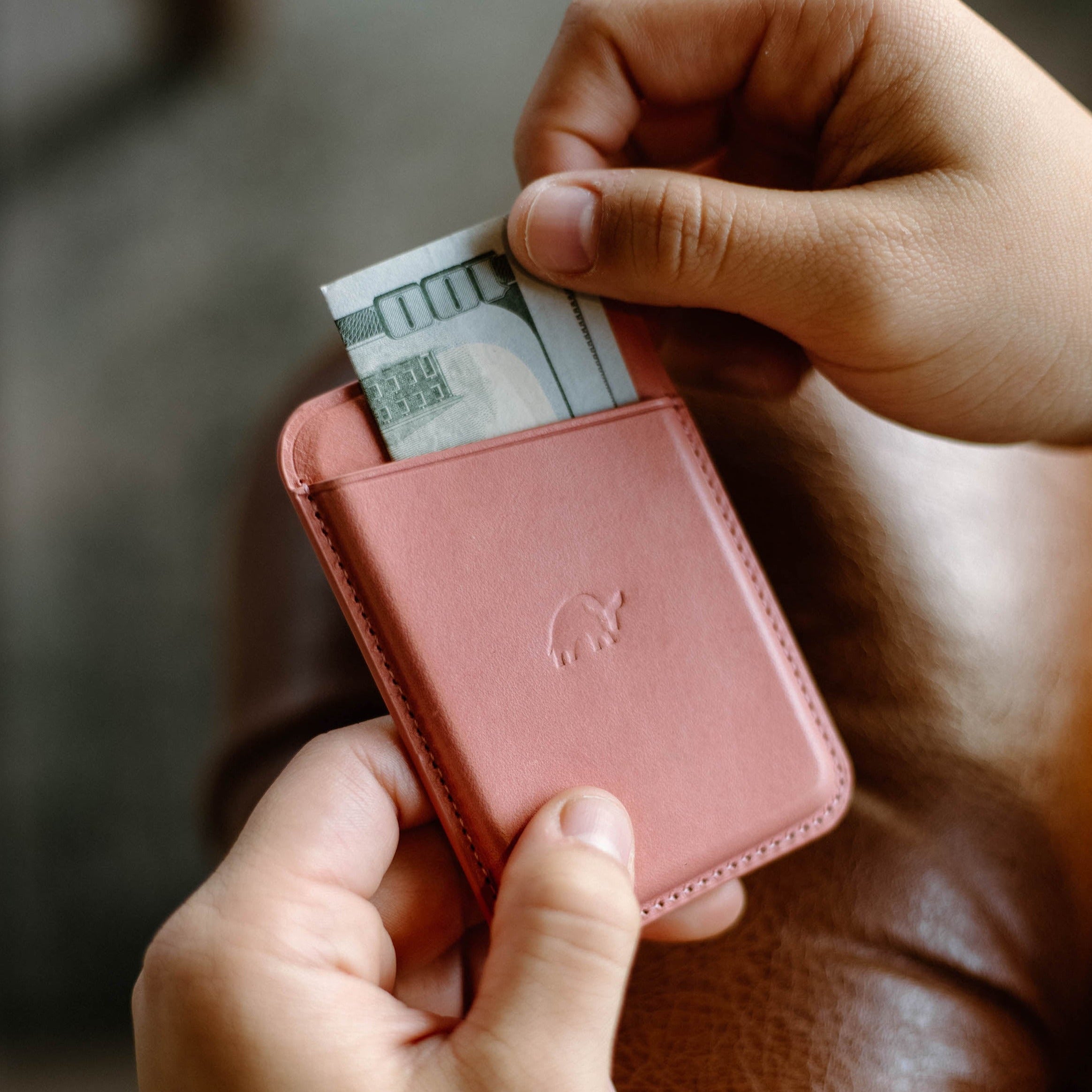 Pink leather magnetic wallet with embossed elephant logo, US bill '100' partly inserted between hands