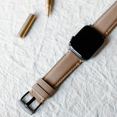 Leather Apple Watch Strap in Dune color, displayed with a pen and metallic objects.