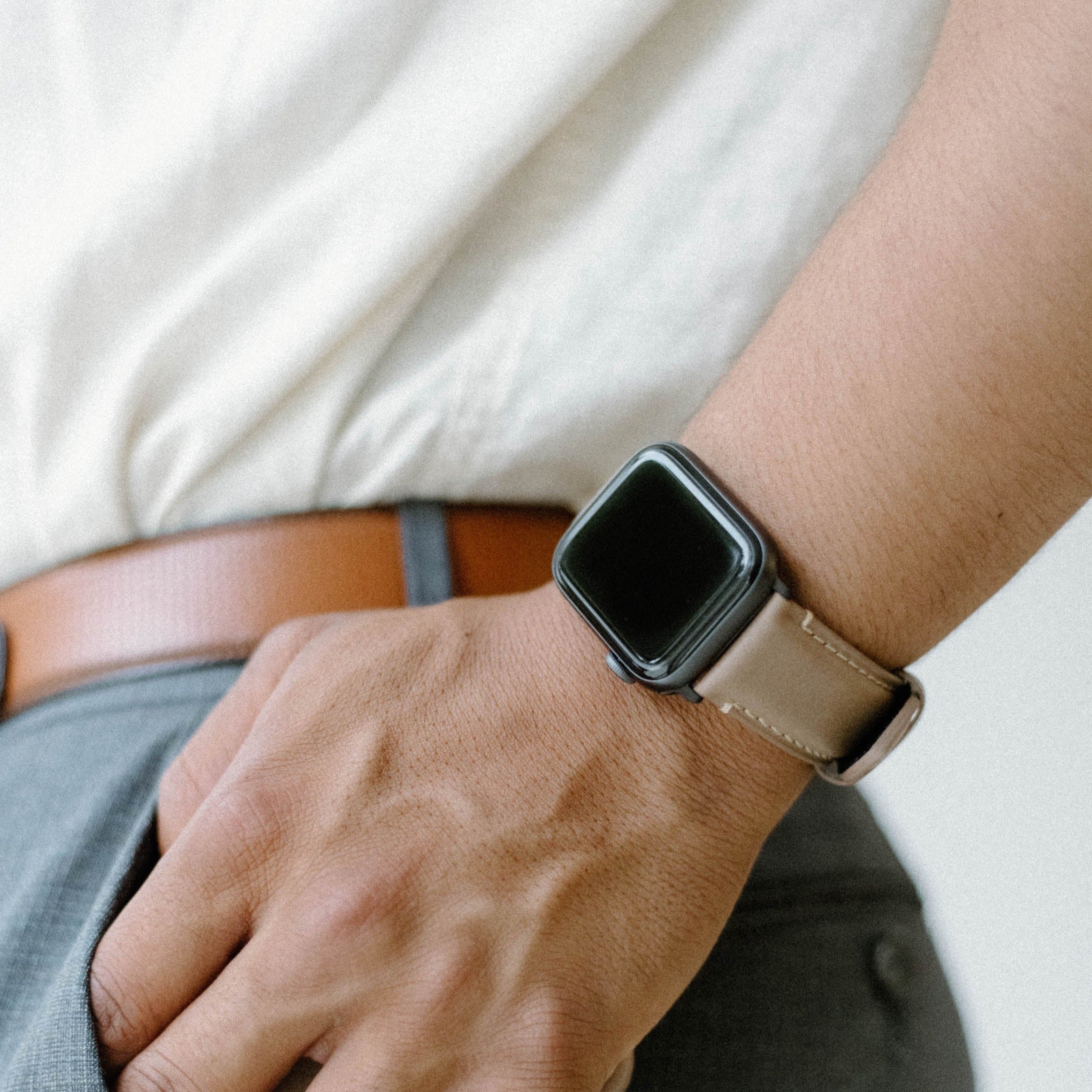Close-up of a hand wearing a leather Apple Watch strap in Dune color.