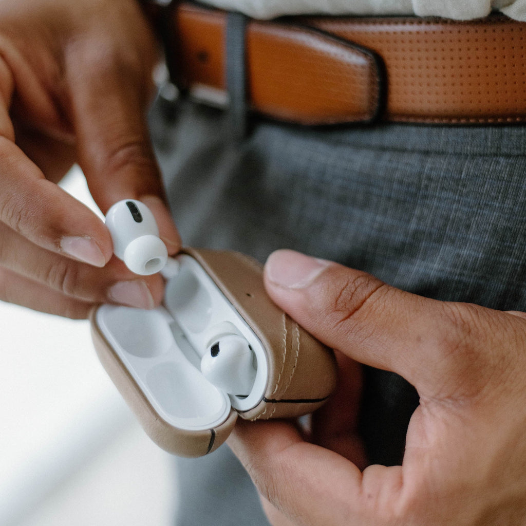 Person holding white wireless earbuds and a tan charging case with one earbud being removed.