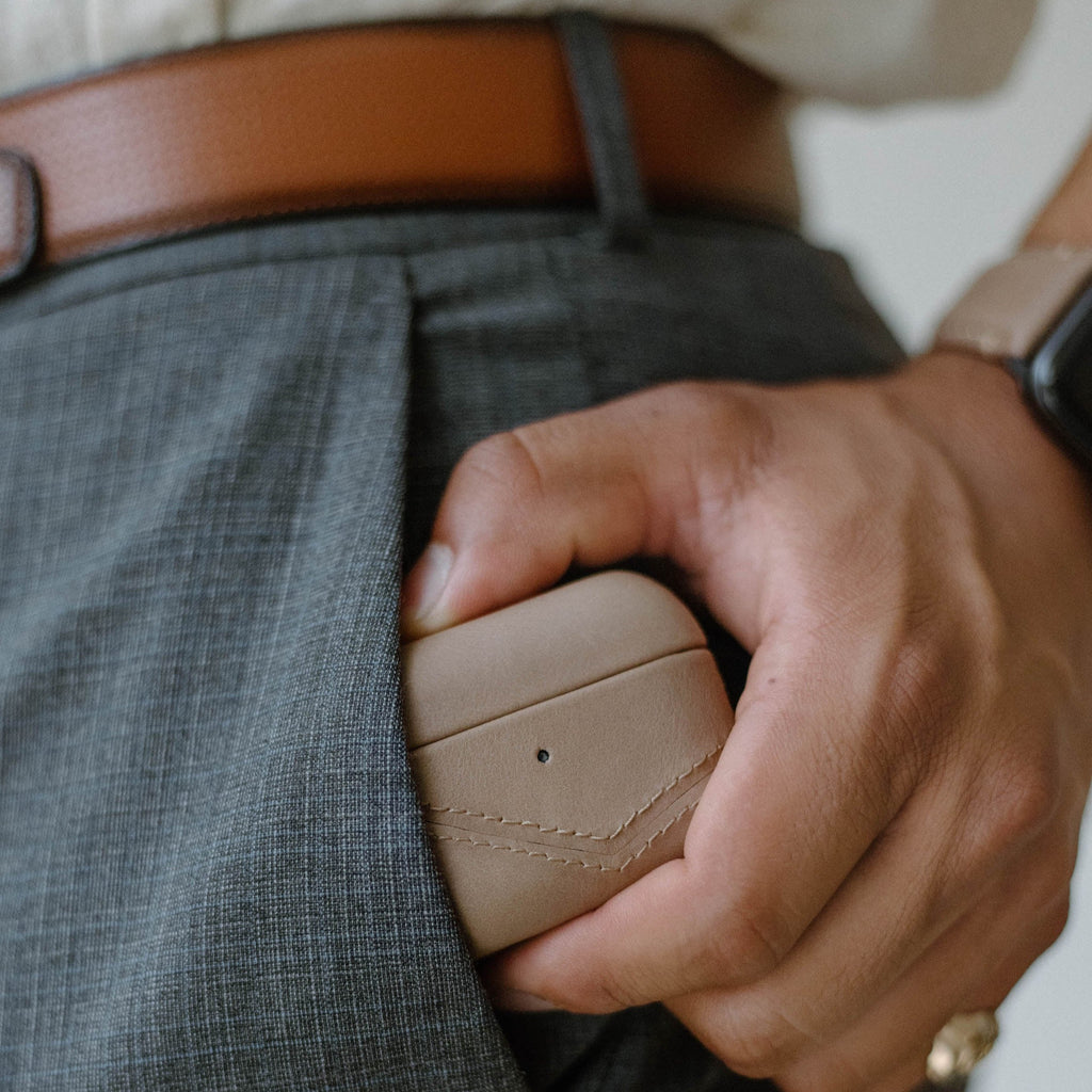 A person holding a beige leather AirPods case in their pocket.