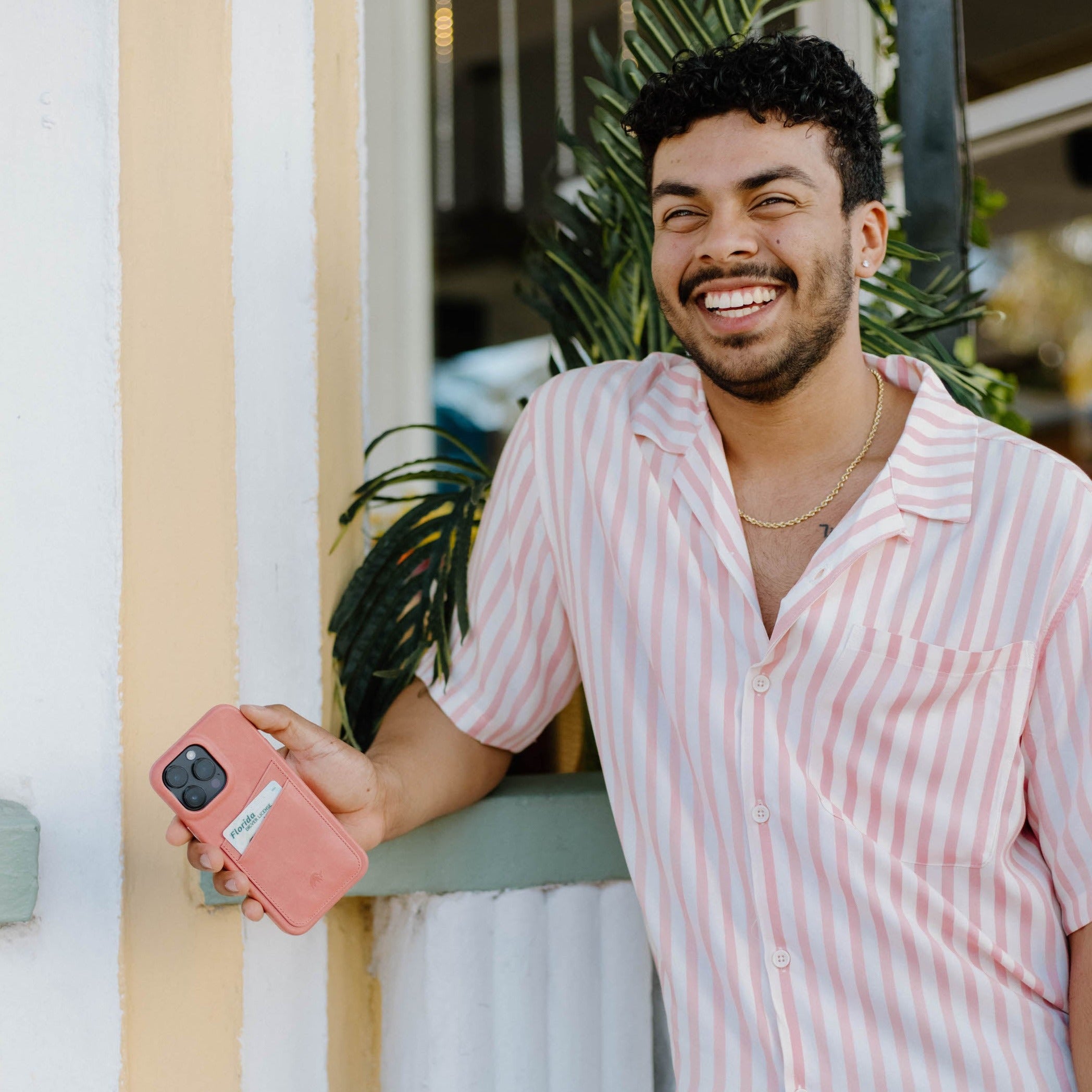 A person smiling while holding the Minimalist Portfolio Case in SOUTH BEACH color, standing near a plant.