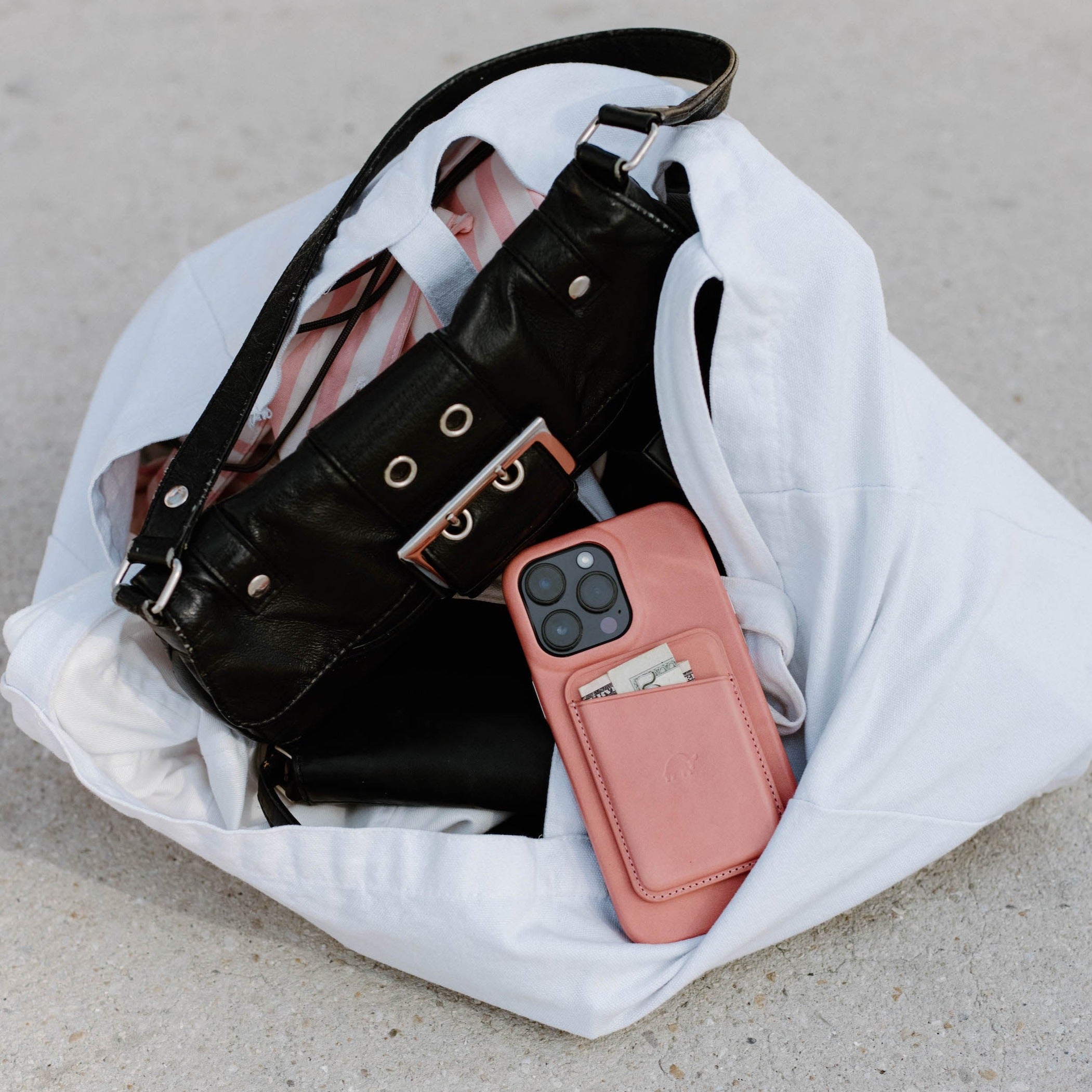 Pink leather wallet-style phone case with card pocket, resting inside a white tote bag next to a black purse