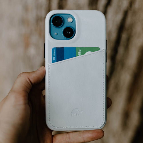 White leather iPhone case with diagonal card pocket holding a blue-green card, held in a hand