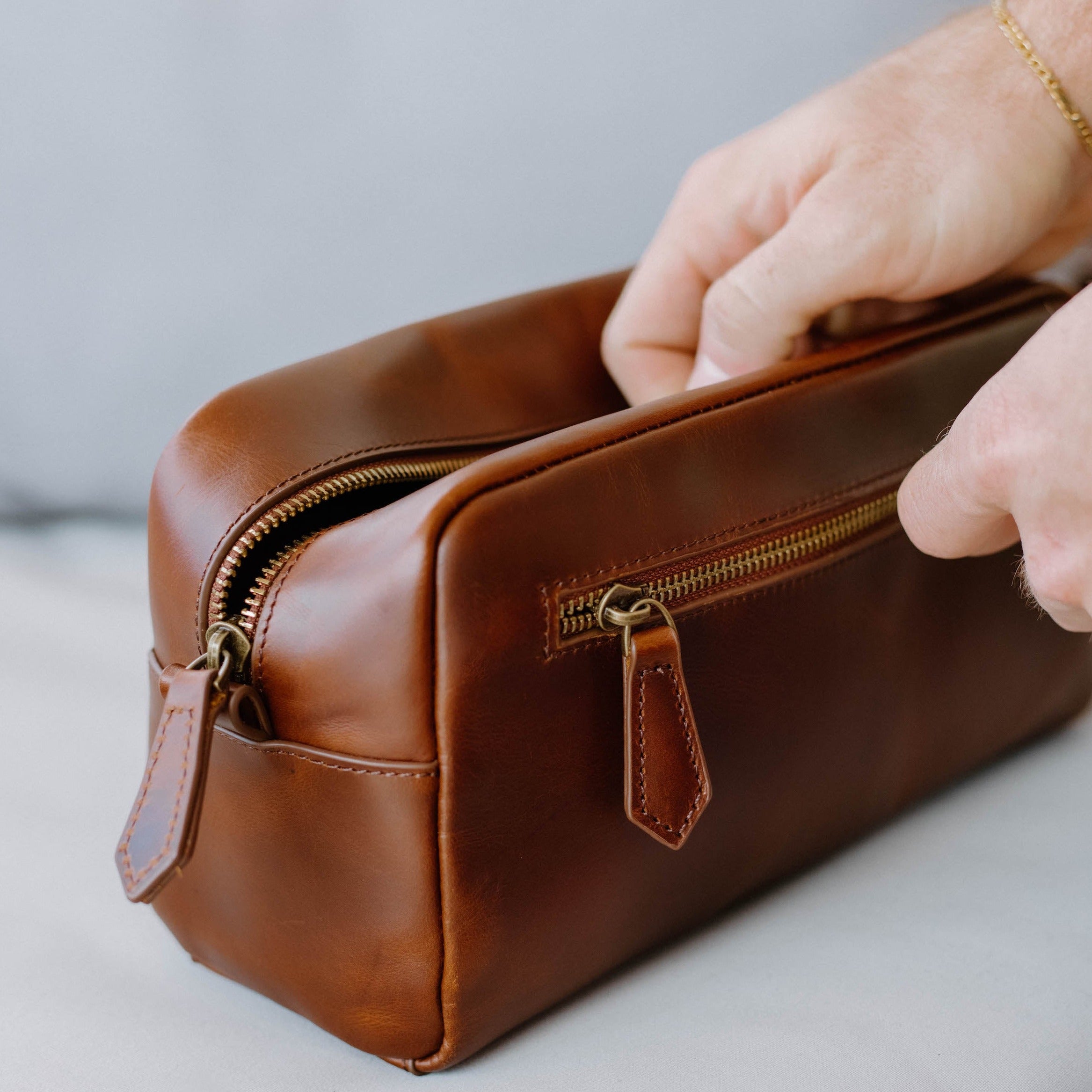 A brown leather toiletry bag with a zipper, being opened.
