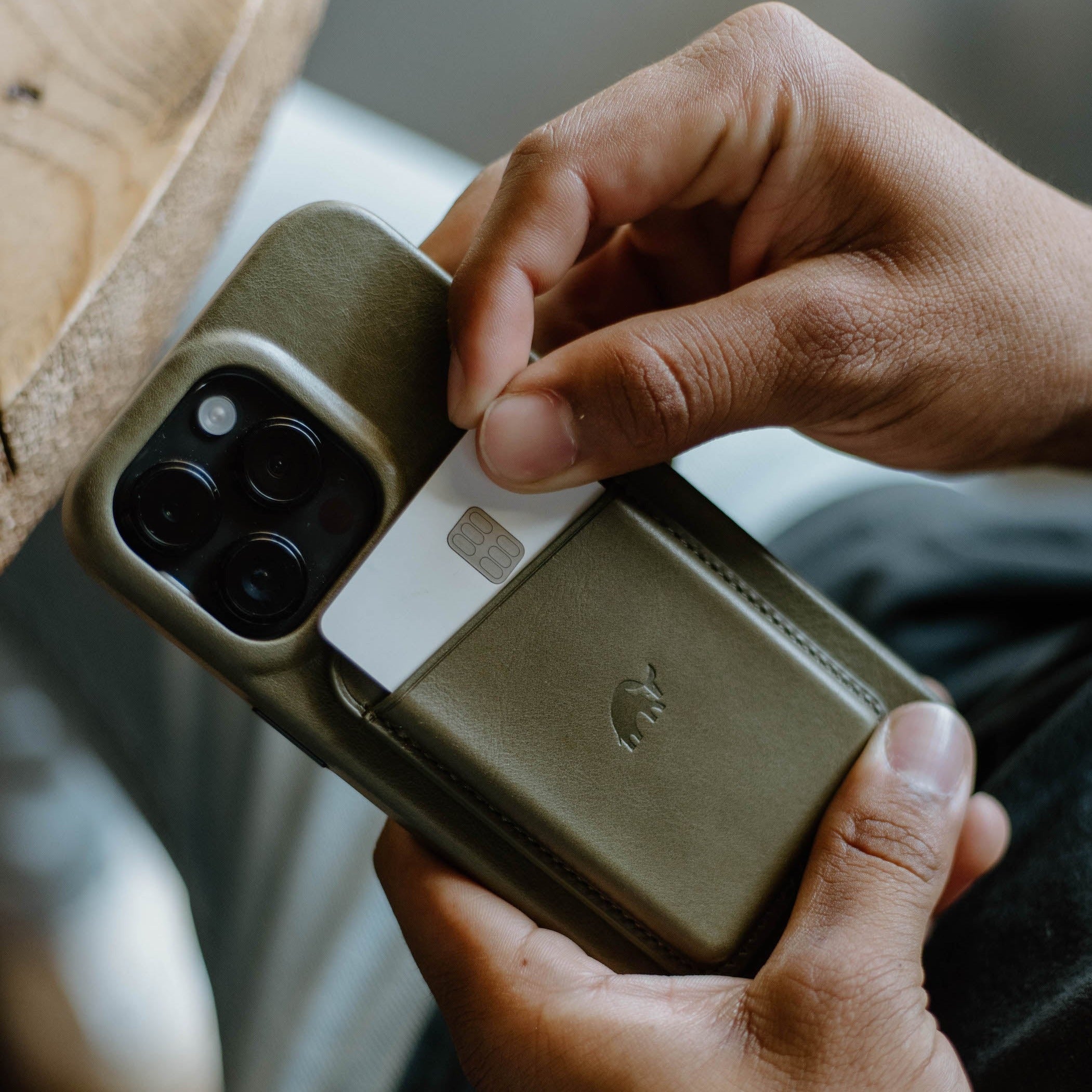 Olive-green leather phone case with stitched card pocket, card partially pulled out and embossed animal logo.