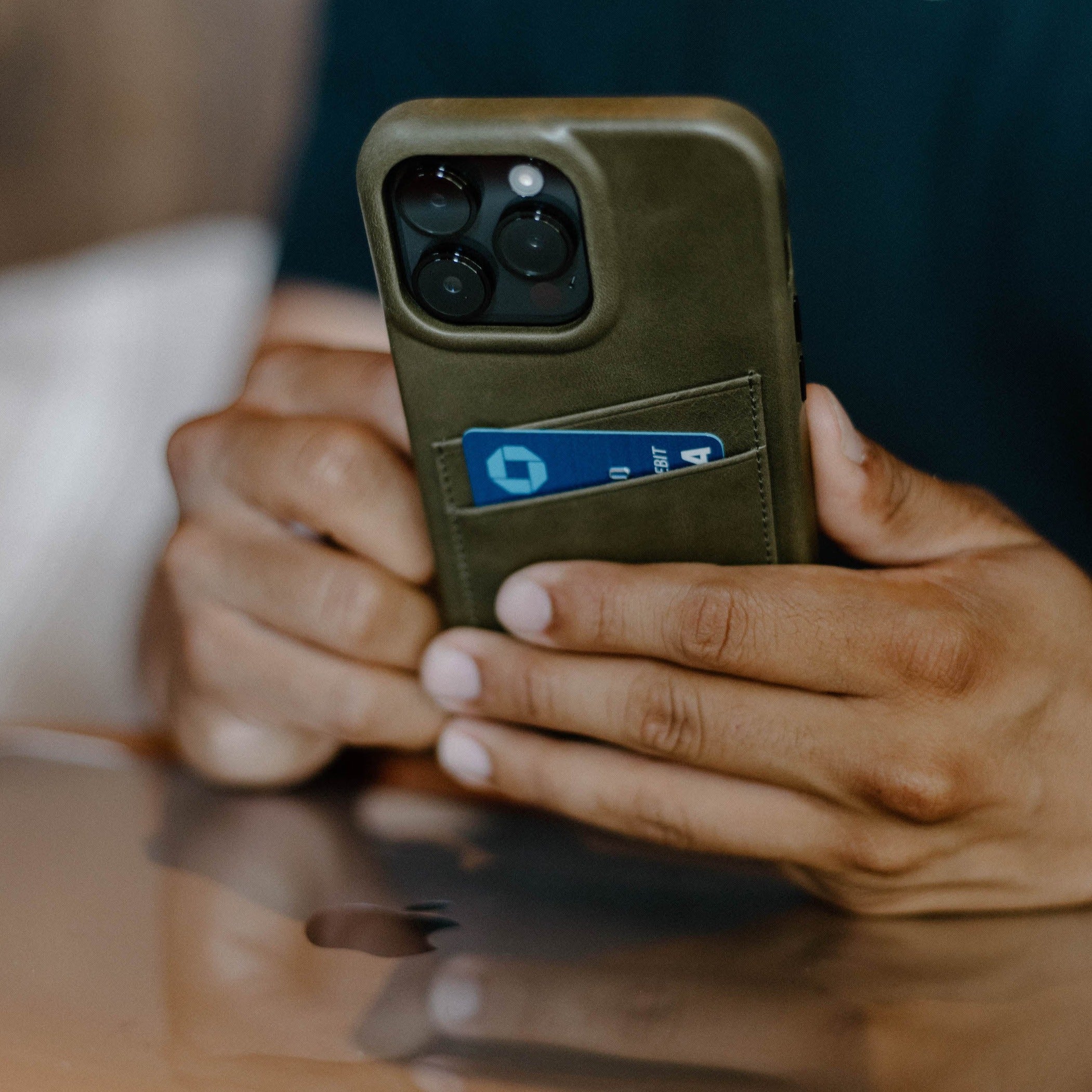 Olive-green leather phone case with two card slots, holding a blue card labeled DEBIT.