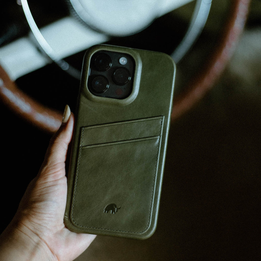 Olive-green leather iPhone case with two card slots and embossed elephant logo, held in a hand