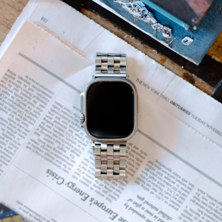 Silver metal Apple Watch with linked stainless-steel bracelet lying on a folded newspaper.