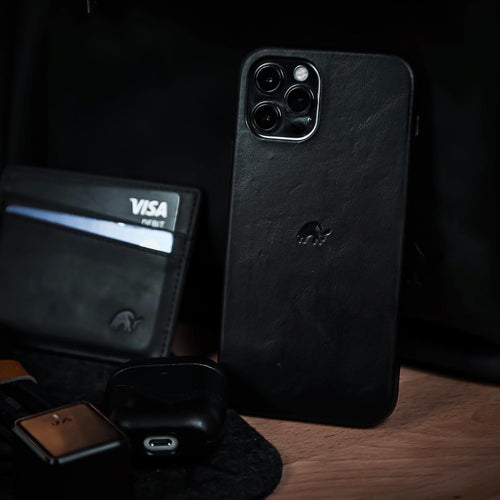 A black leather card holder next to a phone and other accessories on a wooden surface.