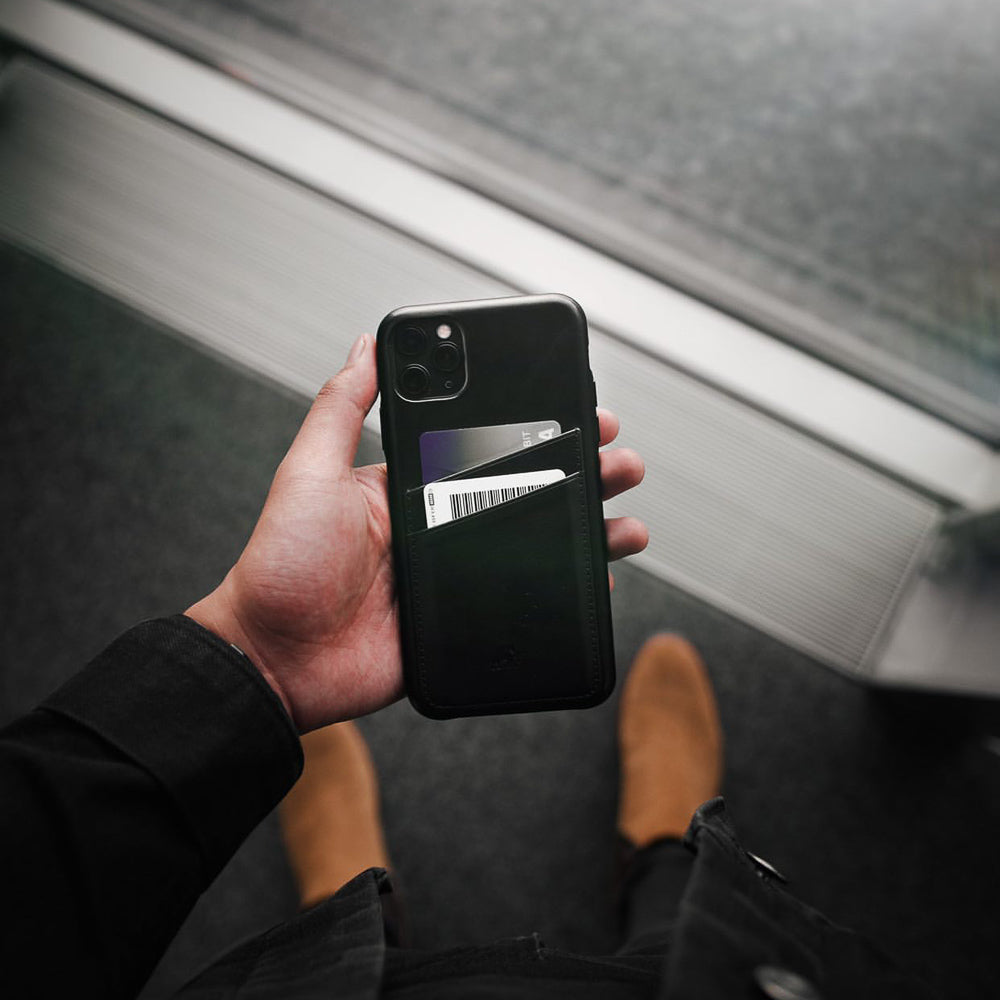 Black phone wallet on a smartphone held in hand, containing two cards; one white card shows a barcode.