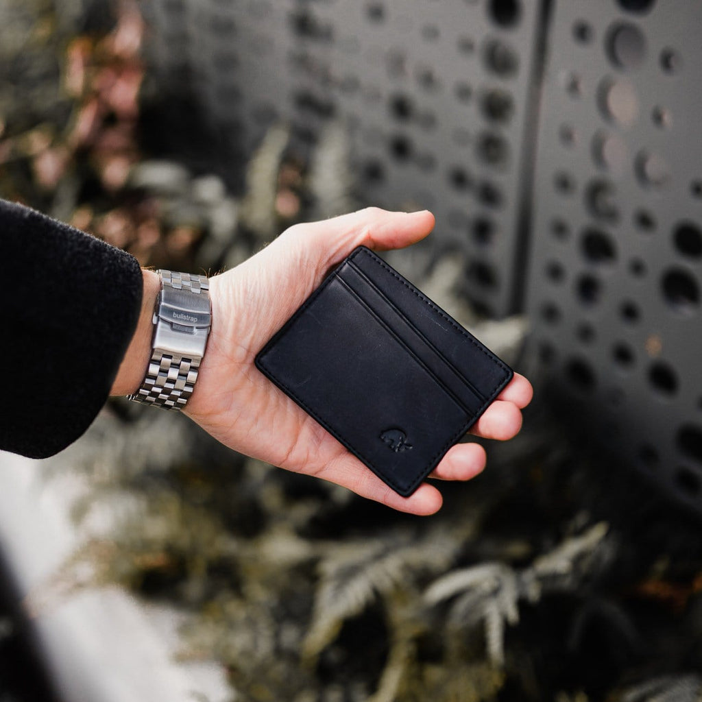 Hand wearing silver metal Apple Watch strap labeled 'bullstrap', holding a black leather card wallet