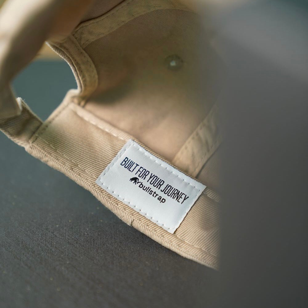 Close-up inside tan cap showing stitched label reading BUILT FOR YOUR JOURNEY and bullstrap logo.