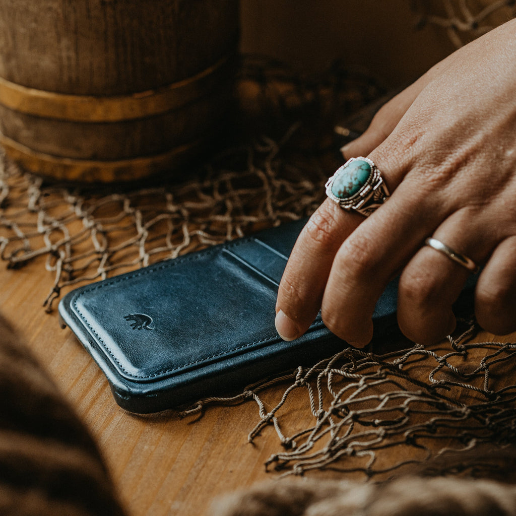 Ocean leather minimalist phone wallet on wooden table, hand with turquoise ring resting on it