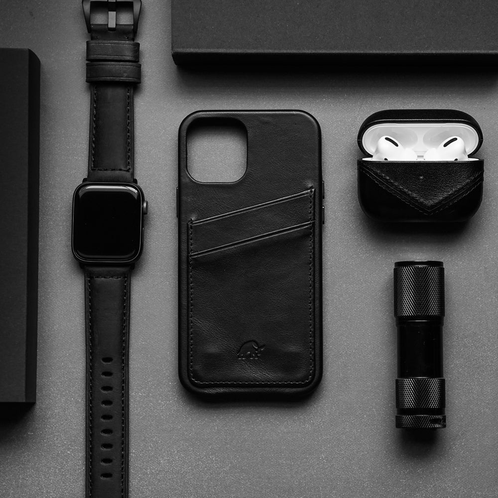 Black flat-lay everyday carry: leather phone card wallet, smartwatch, AirPods in leather case, compact flashlight.