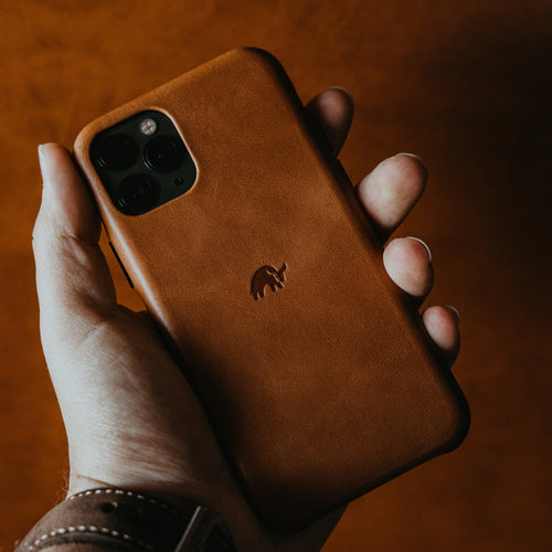 A person holding a brown leather iPhone case with a logo on the back.