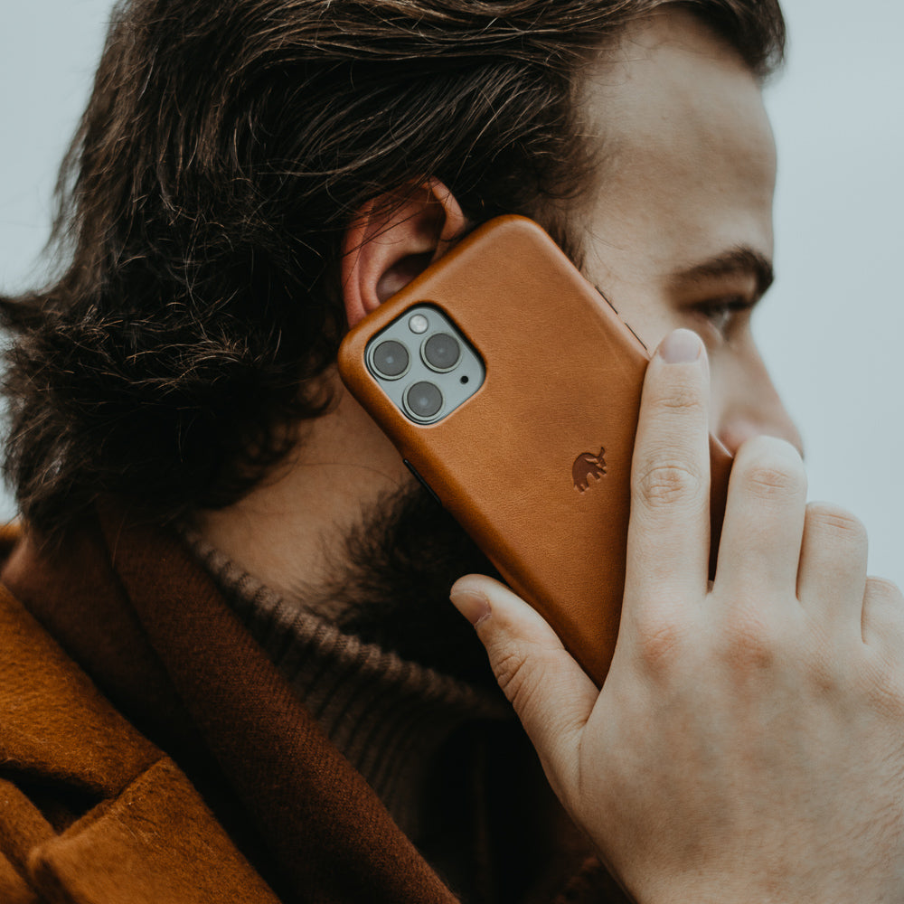 A man holding a leather iPhone case to his ear, showcasing its design.