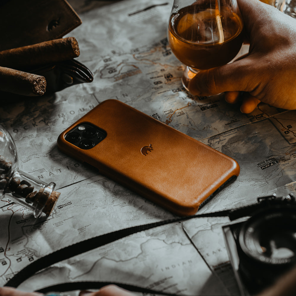 A brown leather iPhone case on a map with a glass of drink nearby.