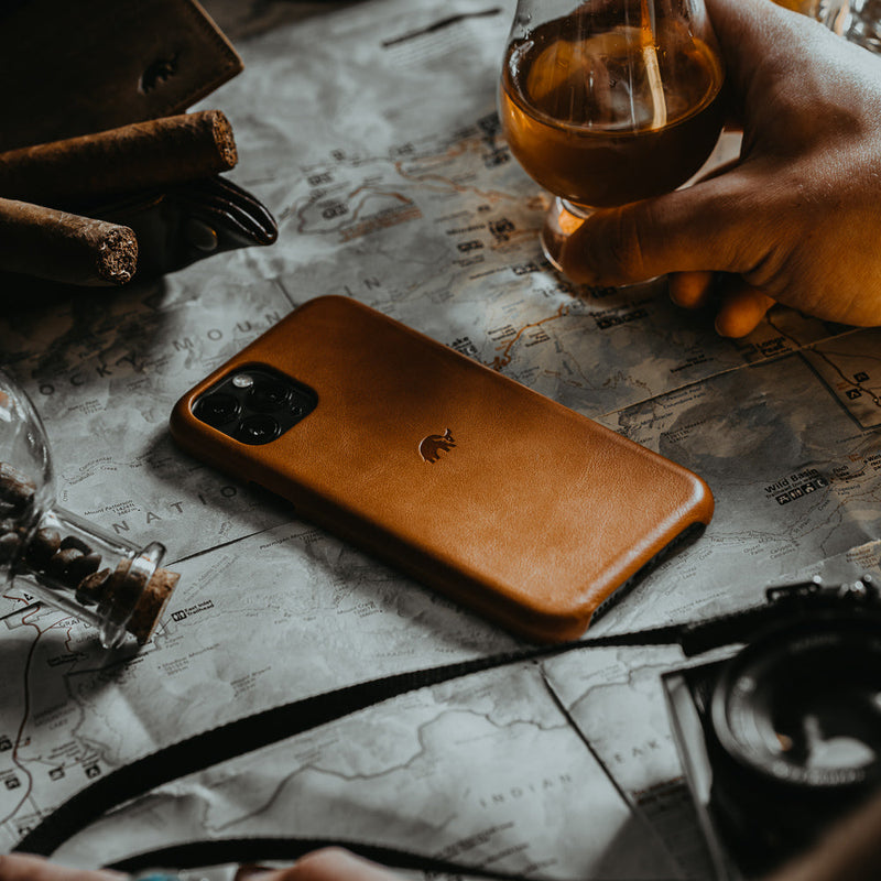 A brown leather iPhone case on a map with a glass of drink nearby.