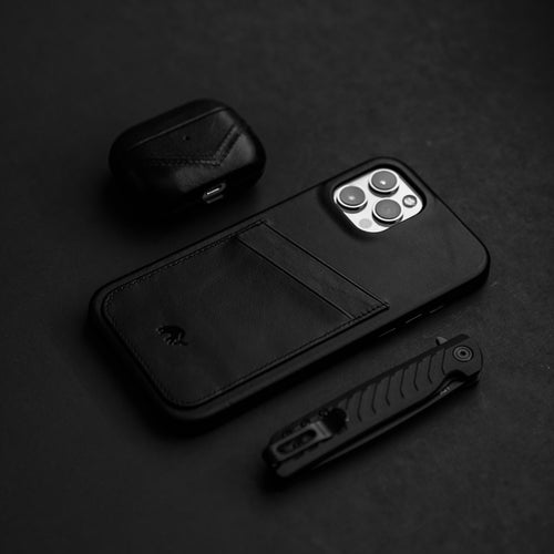 A black minimalist portfolio case with card slot, an AirPods case, and a knife on a dark surface.