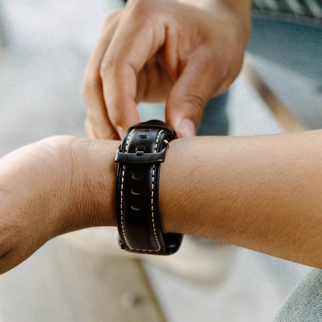 A person adjusting a leather Apple Watch strap on their wrist.
