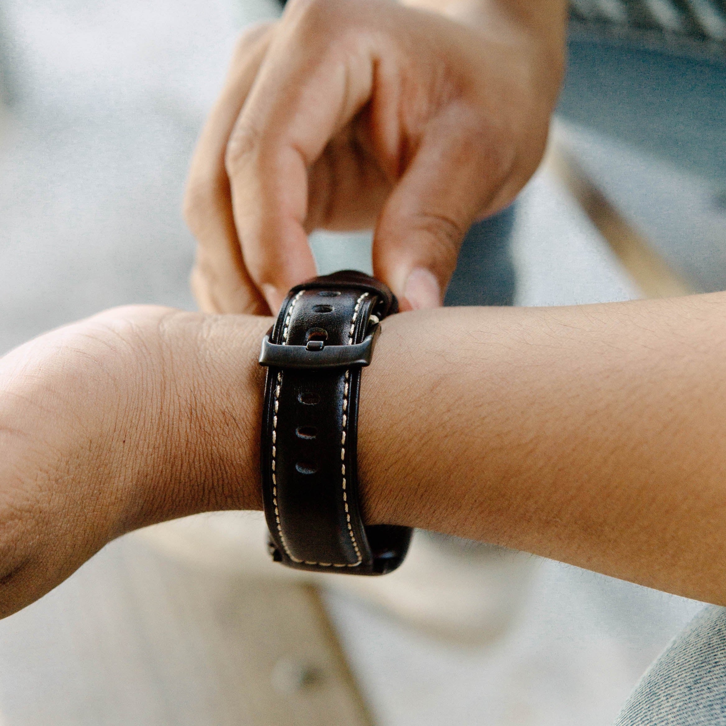 A person adjusting a leather Apple Watch strap on their wrist.