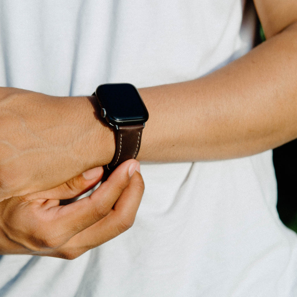 A person wearing a brown leather Apple Watch strap on their wrist.