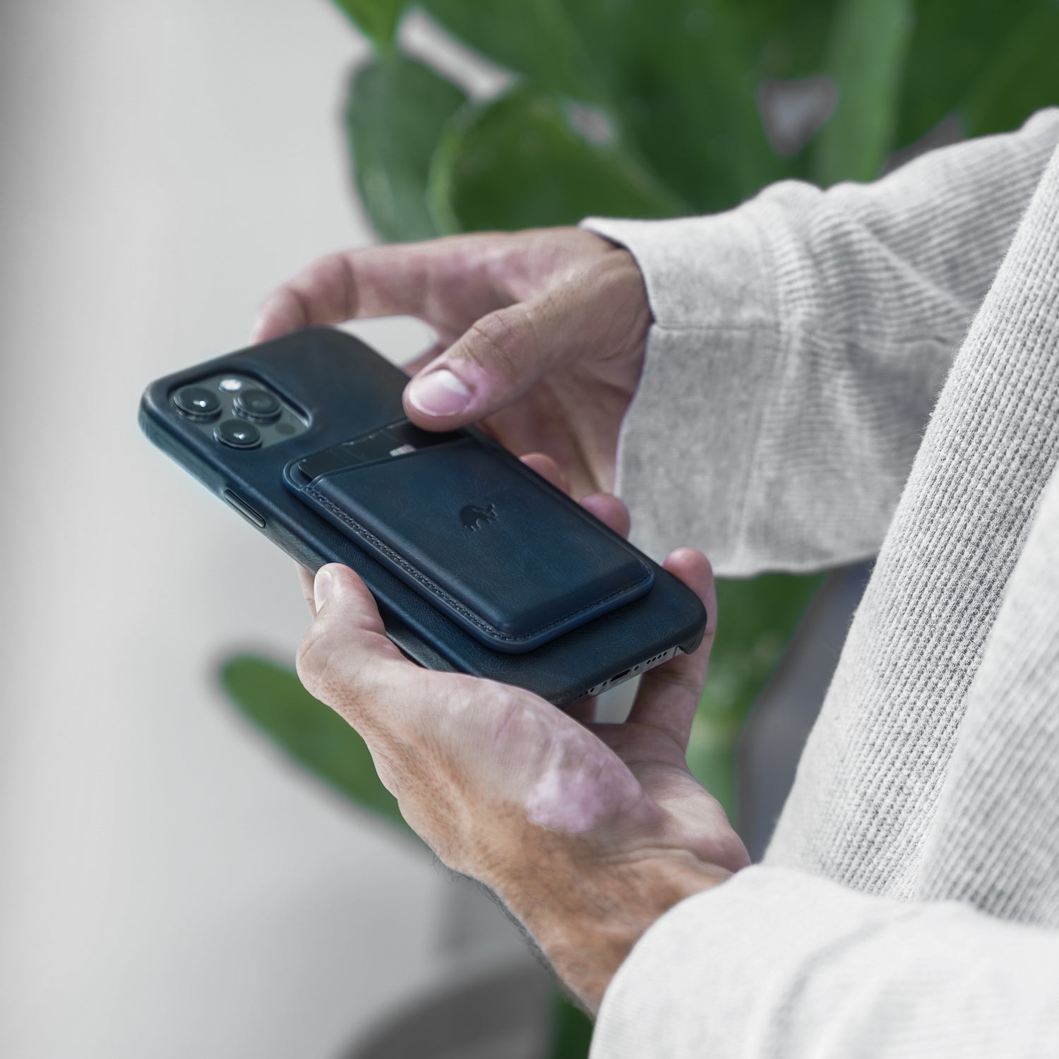 A person holding a phone with a slate leather magnetic wallet attached to it.