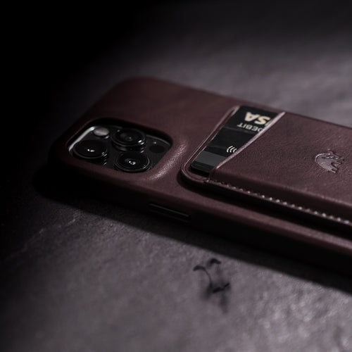 iPhone case with attached bourbon leather magnetic wallet holding a card labeled DEBIT and VISA, contactless symbol visible