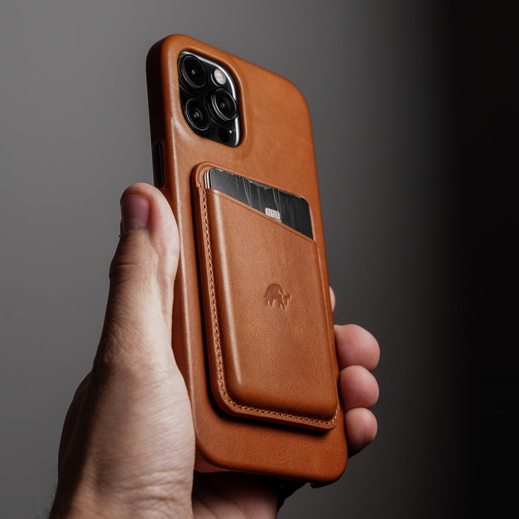 A person holding a leather magnetic wallet in sienna color, attached to a phone case, with a card visible in the wallet.