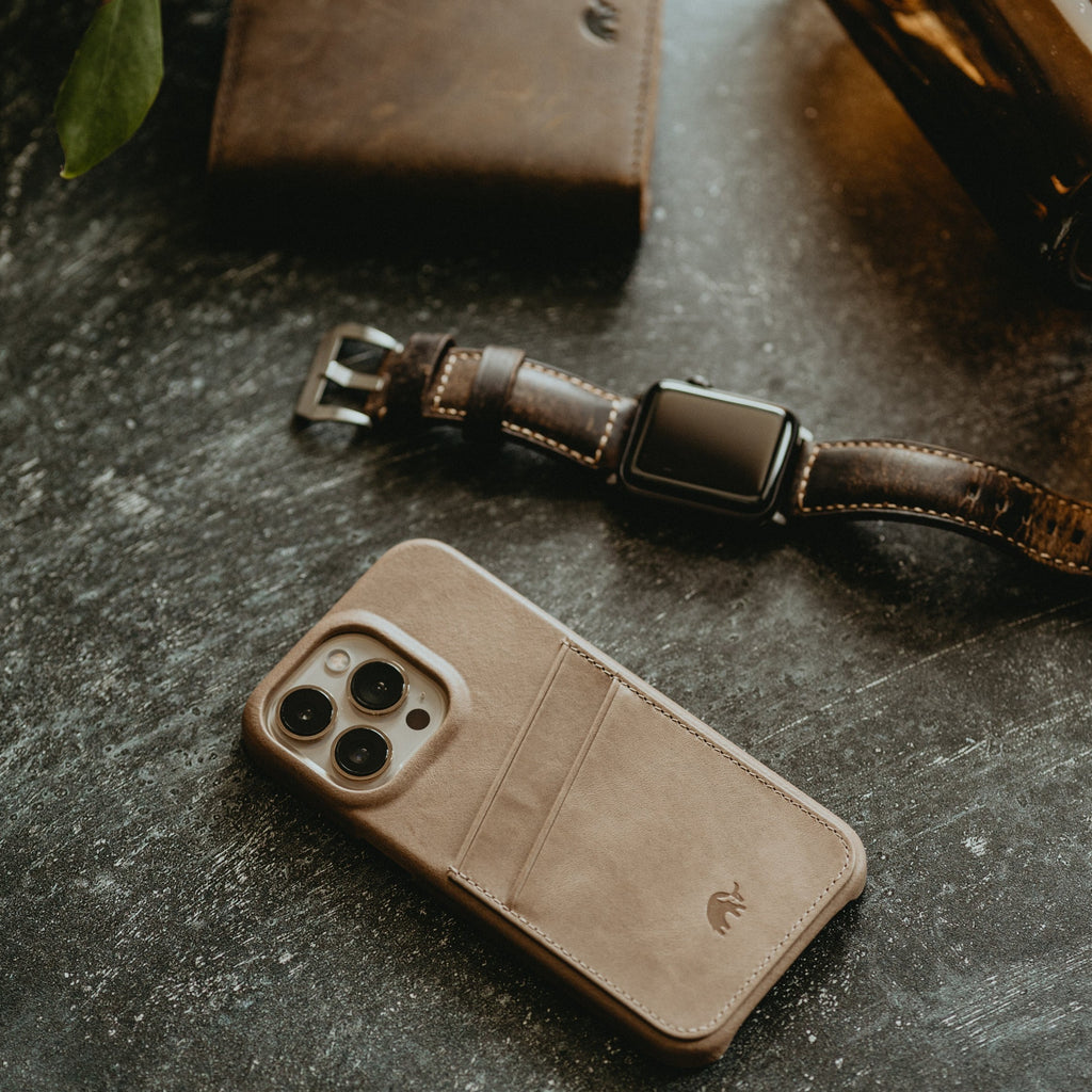 The Minimalist Portfolio Case in Dune color, displayed with a watch and wallet on a textured surface.