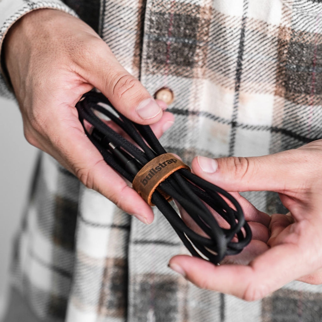A person holding a bundled black charging cable with a leather tie.