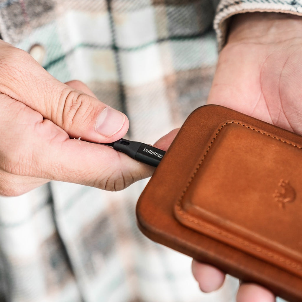 A person connecting a charging cable to a Bullstrap wallet.