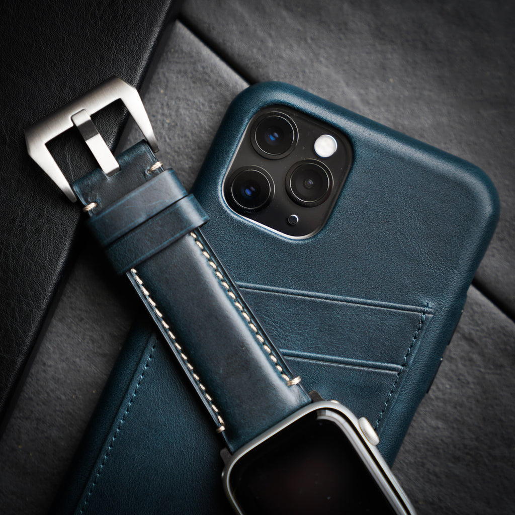 Teal leather phone wallet case with diagonal card slots beside matching leather watch strap and smartwatch.